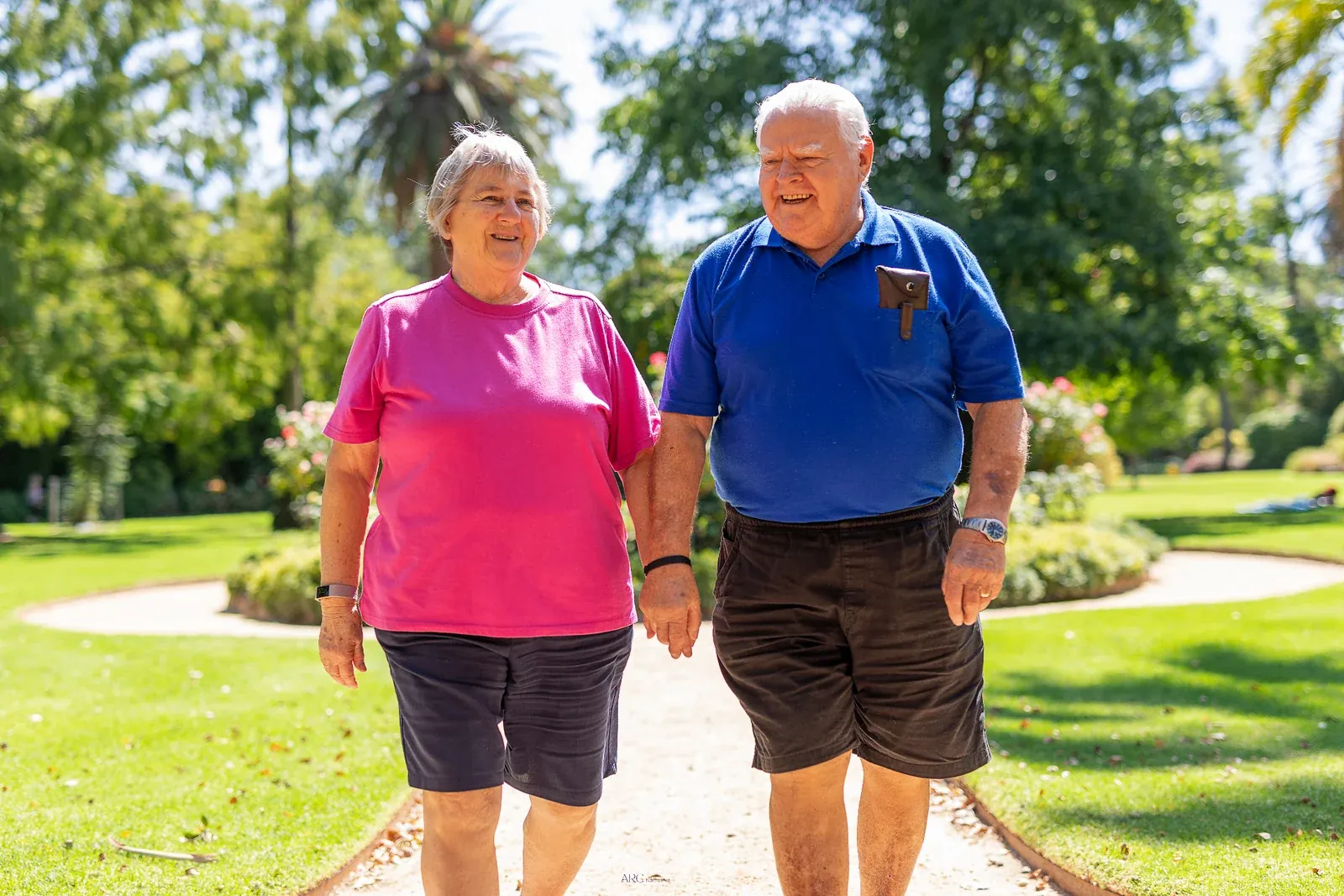 Older couple walking together through a sunny garden, illustrating retirement living